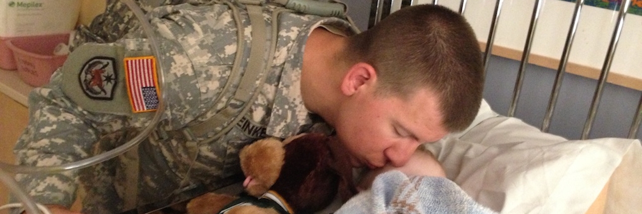 A Letter to the Husbands Who Support Moms of Sick Children A dad leans over his son in bed and kisses his head