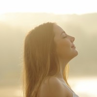 Woman breathing deep fresh air in the morning sunrise
