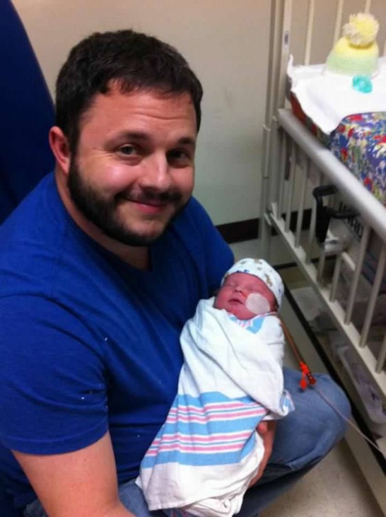 Dad smiling at camera while holding baby at hospital