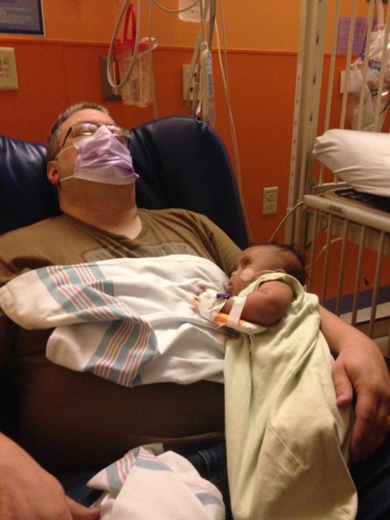 Dad sleeping with face mask on while holding baby in hospital