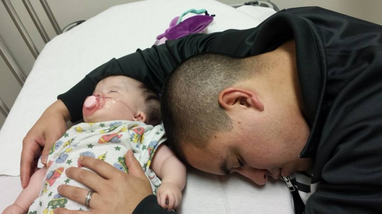 Dad holding and sleeping next to baby in hospital bed