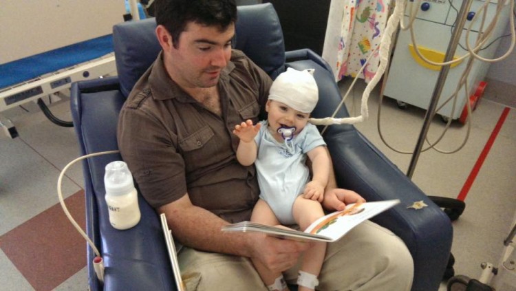 Dad reading to baby in hospital chair, baby smiling and holding arm up