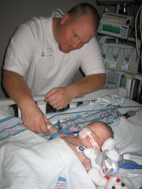 Dad holding hand of baby on hospital bed