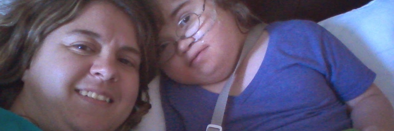 Imagining Special Needs Parenting as a Reality Show woman laying down next to her daughter playing on an ipad