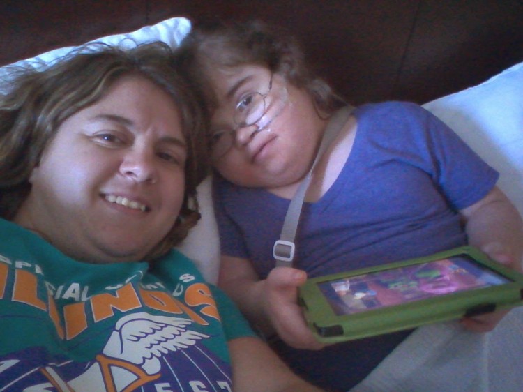 woman laying down next to her daughter playing on an ipad