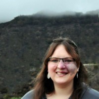 A woman with a birthmark on her face stands with the Hollywood sign in the background