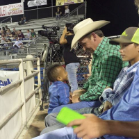 The author's son standing in front of man at rodeo