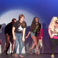 A young woman performs song on stage with a group of young people