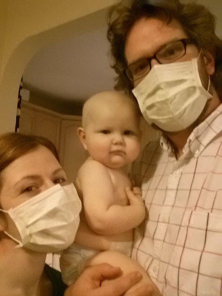 husband and wife in doctor's masks holding baby