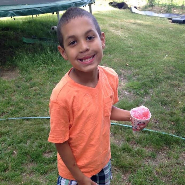 A small boy in a t-shirt, shorts and sneakers holds a snocone as he stands on the grass