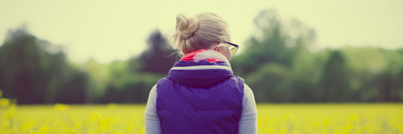 What I Wouldn’t Have Achieved Without Chronic Illness Back view of woman wearing glasses and looking at field of yellow flowers