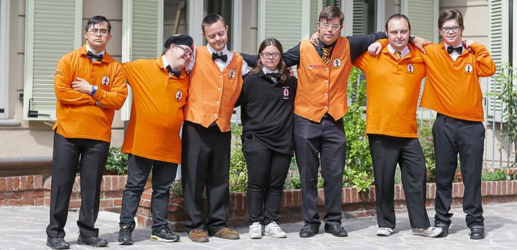 Group photo of the employees outside the hotel wearing orange uniforms.