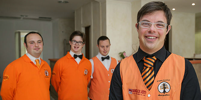 The employees stand in the hotel, smiling with orange uniforms. 