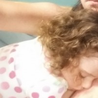 A mom sits with her toddler daughter sleeping on her chest