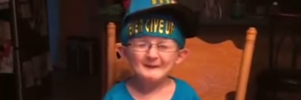 Boy With Schwartz-Jampel Syndrome Makes Video After Meeting John Cena A boy with glasses and wearing a hat sitts at a table as he talks into the camera