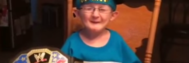 A boy with glasses and wearing a hat sitts at a table as he talks into the camera