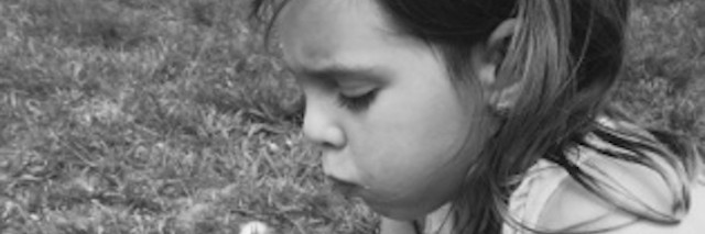 Black and white photo of a girl holding a dandelion and blowing on it