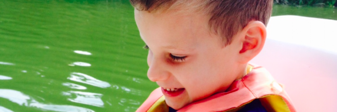 What It's Like to See My Child With Epilepsy Fail His Medication Young boy wearing a lifejacket and smiling in a boat on a green lake