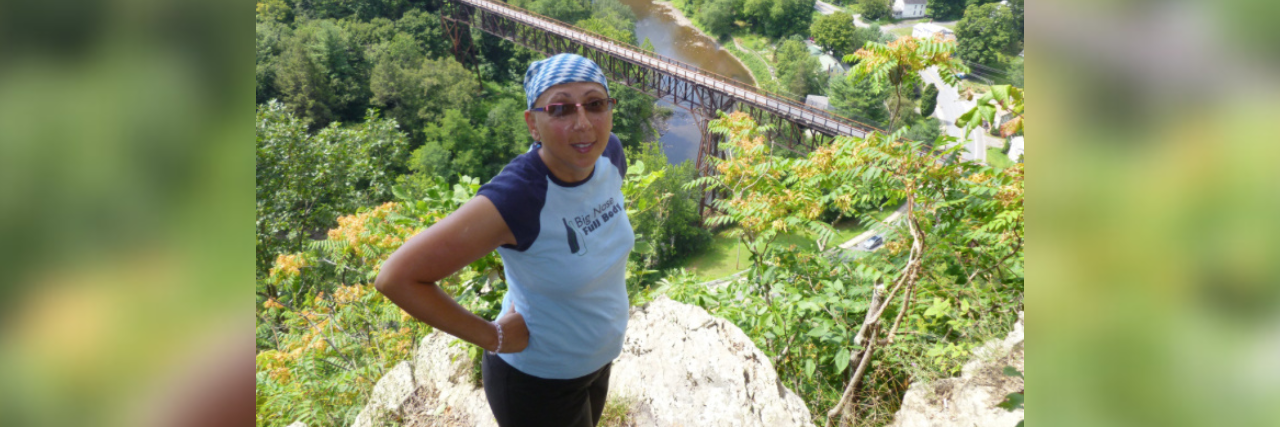 Why My Life as a Cancer Survivor Feels Like a Ticking Time Bomb Contributor wearing a scarf and sunglasses outside on hiking trail with view of trees behind her