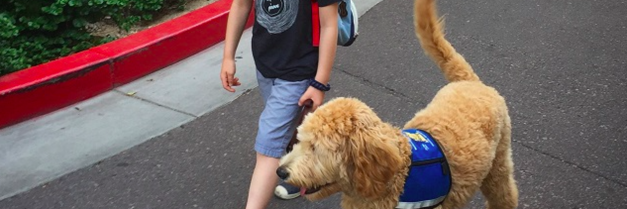 A young boy walking with his service dog and wearing a backpack