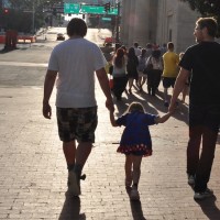 A little girl walking an holding hands with her brothers on either side of her