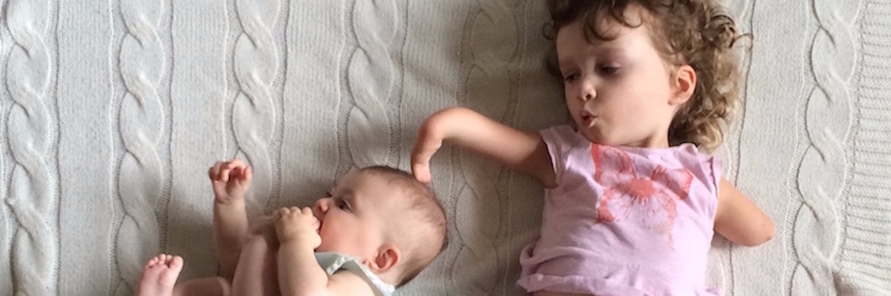 young girl with a limb difference lays next to her baby sister