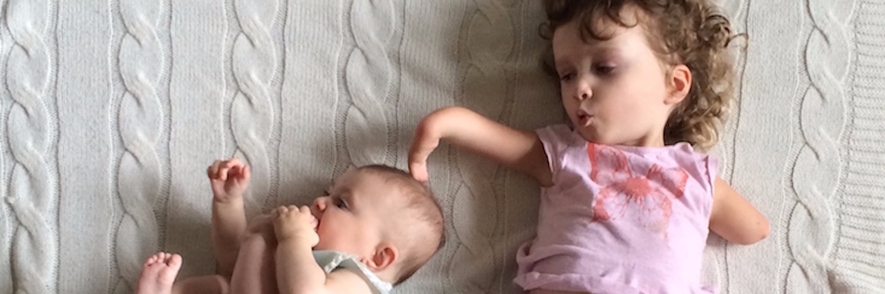 Shoe Shopping for My Daughter With Limb Differences young girl with a limb difference lays next to her baby sister