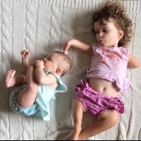 young girl with a limb difference lays next to her baby sister