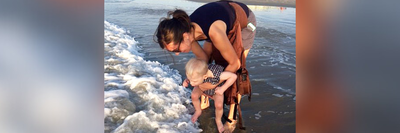 Mother holding child to dip their toes in the water at the beach