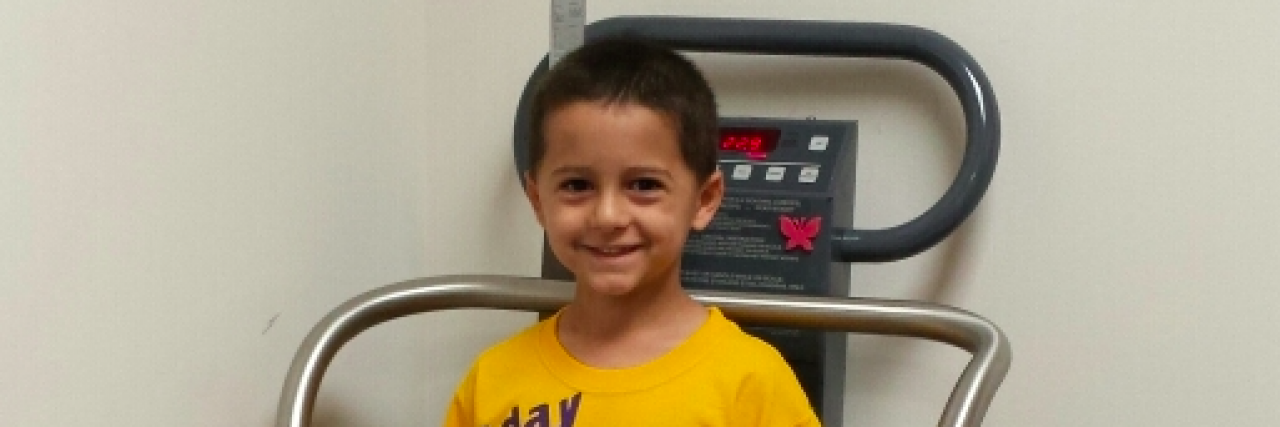 Young boy smiling and wearing a yellow tshirt that says "Today is my last chemo"