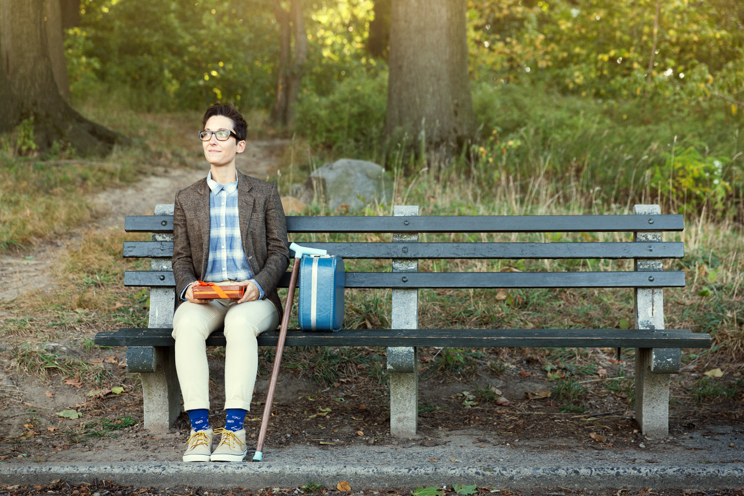 Liz Jackson poses on a bench outside with cane and a briefcase