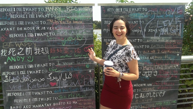 woman standing next to a chalkboard where people have written what they want to do before they die