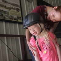 A mom looking down at her daughter, who is wearing a helmet and looking away