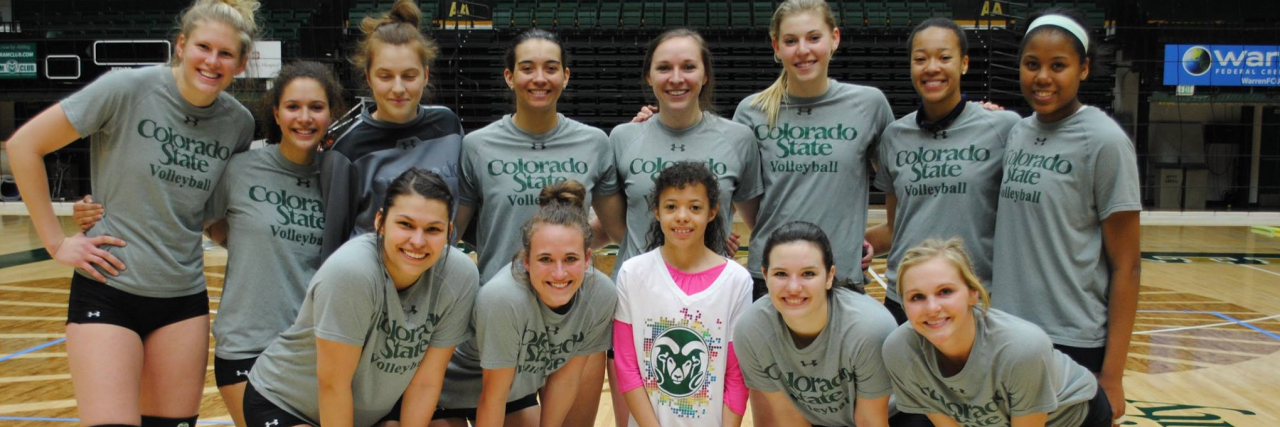 the Colorado State University women's basketball team smiles for the camera with a young girl on their court