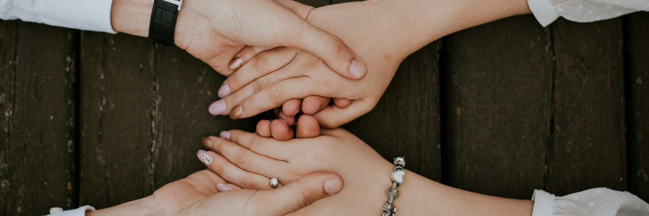 The Words That Changed My Outlook on Living With Bipolar Disorder Two women's arms with holding hands across a wood table wearing white shirts.