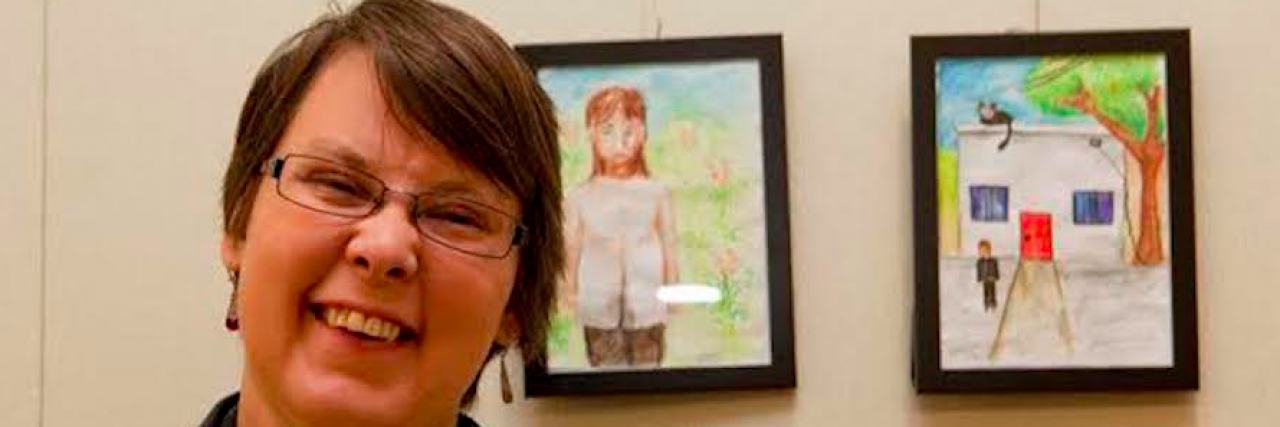 Contributor, a white woman with short hair, smiling with two pieces of artwork behind her