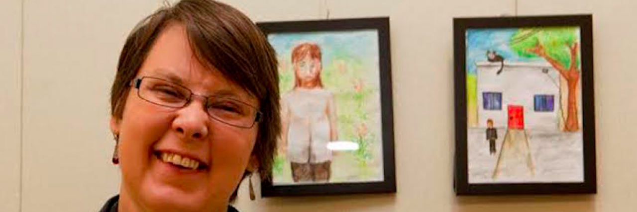 Why I Lived Openly With Autism While Hiding My Schizophrenia Contributor, a white woman with short hair, smiling with two pieces of artwork behind her