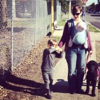 woman wearing baby carrier and walking with boy and dog on street