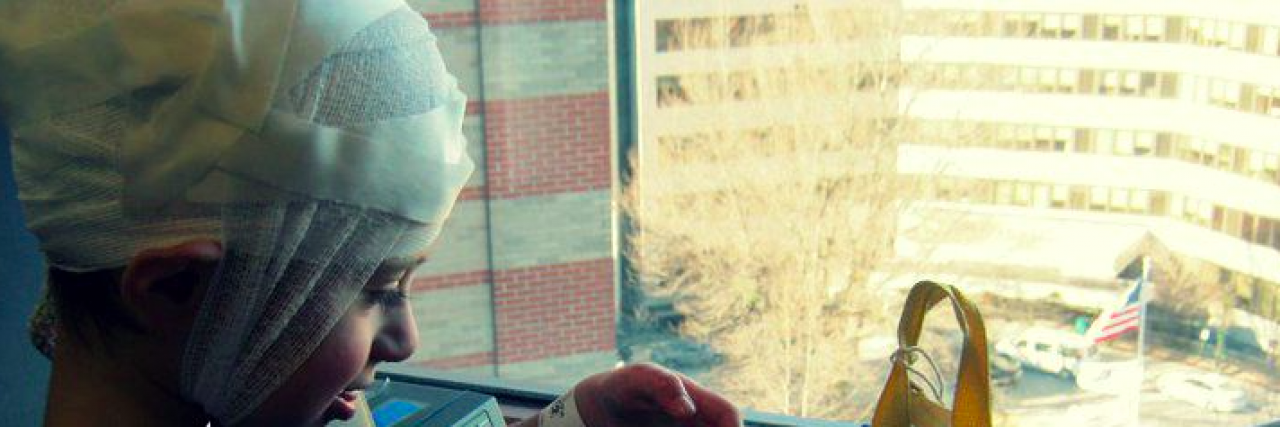 How to Survive an Inpatient EEG (Like a Boss) Child slightly smiling with head wrapped up and opening backpack in hospital room