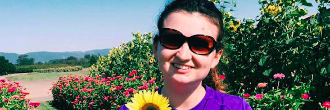 5 Things I Wish Parents Knew About Respite Caregivers Woman holding a flower surrounded by gardens, wearing sunglasses, and smiling