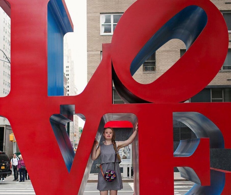 Madeline Stuart posing in between the V and E in a large red LOVE sign