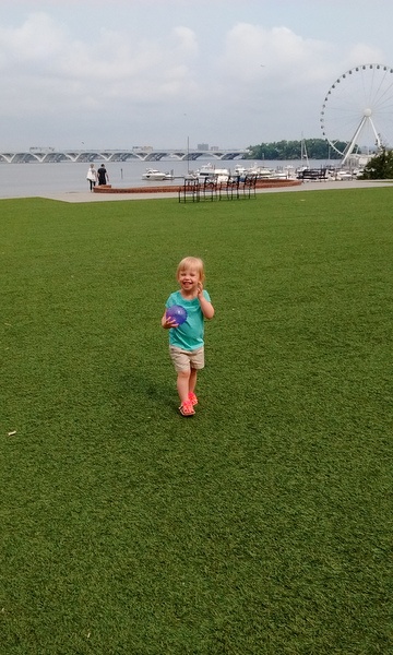 Little girl holding a ball in a field of grass.