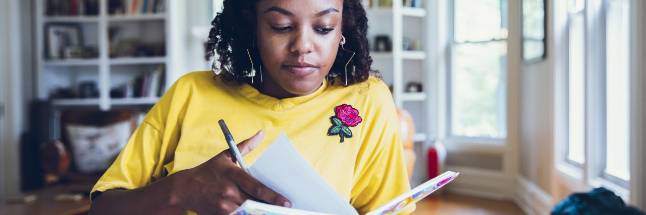 Young black woman holding a pen and flipping through pages in a colorful notebook.