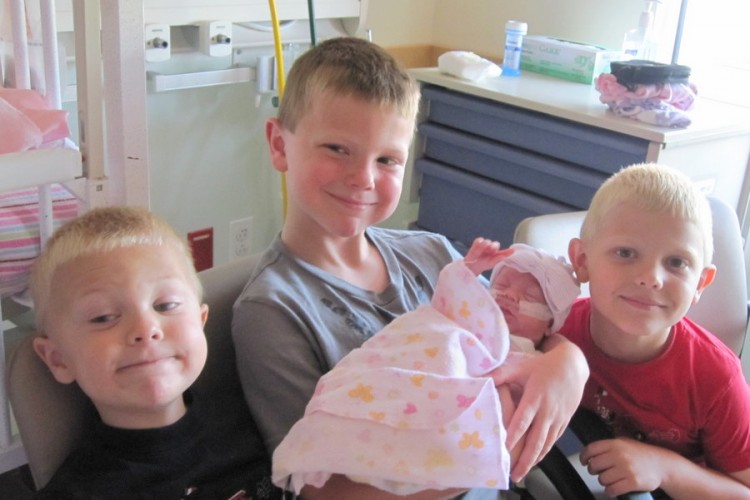 three young boys holding their baby sister in the NICU