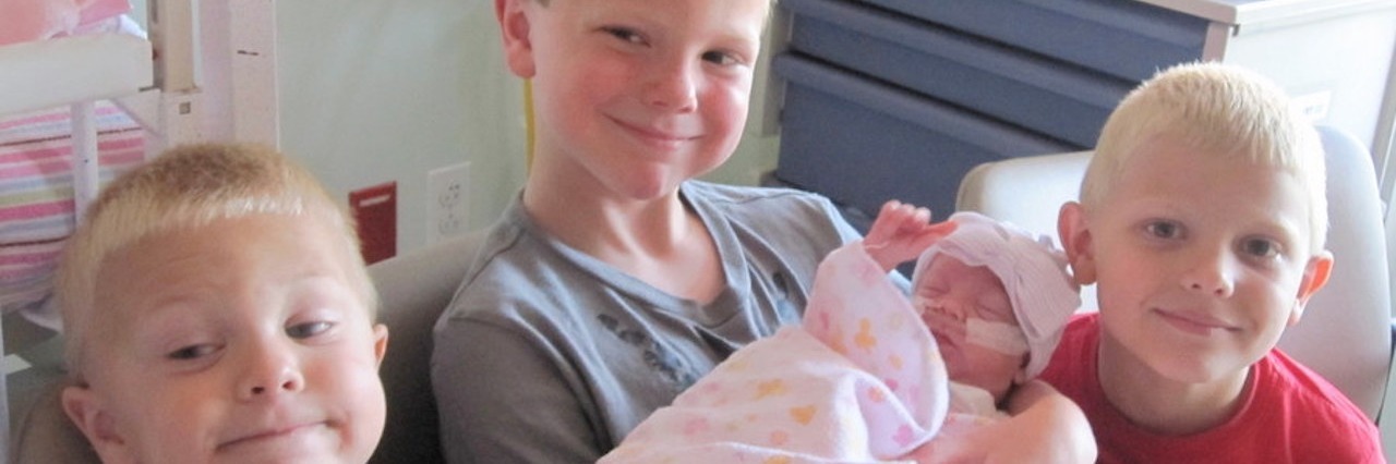 Helping Children Connect With Their Baby Sibling in the NICU three boys holding their baby sister in the NICU