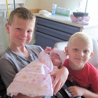 three boys holding their baby sister in the NICU