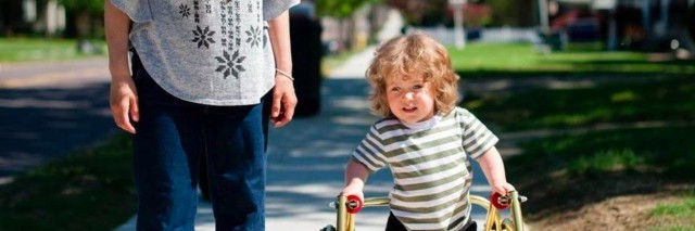 boy with walker walking down street with mom