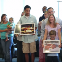 Families stand in a line with their children holding pictures of themselves from when they were in the NICU as babies