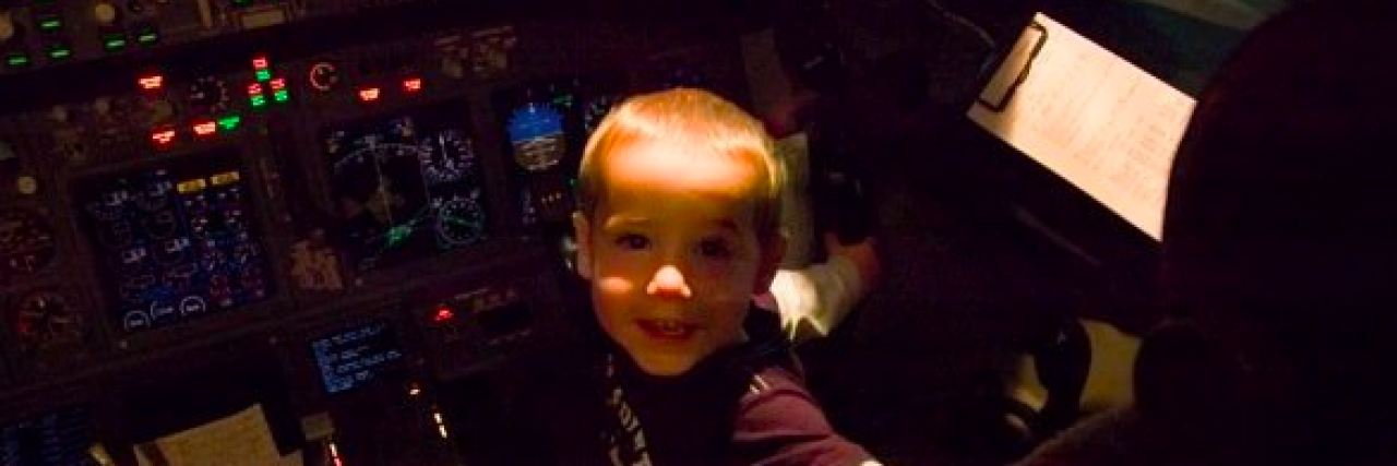 Young boy sitting in airplane cockpit in front of control panels and smiling widely