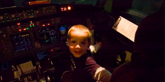 Young boy sitting in airplane cockpit in front of control panels and smiling widely